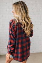 Woman wearing a red and black plaid shirt against a white brick wall.
