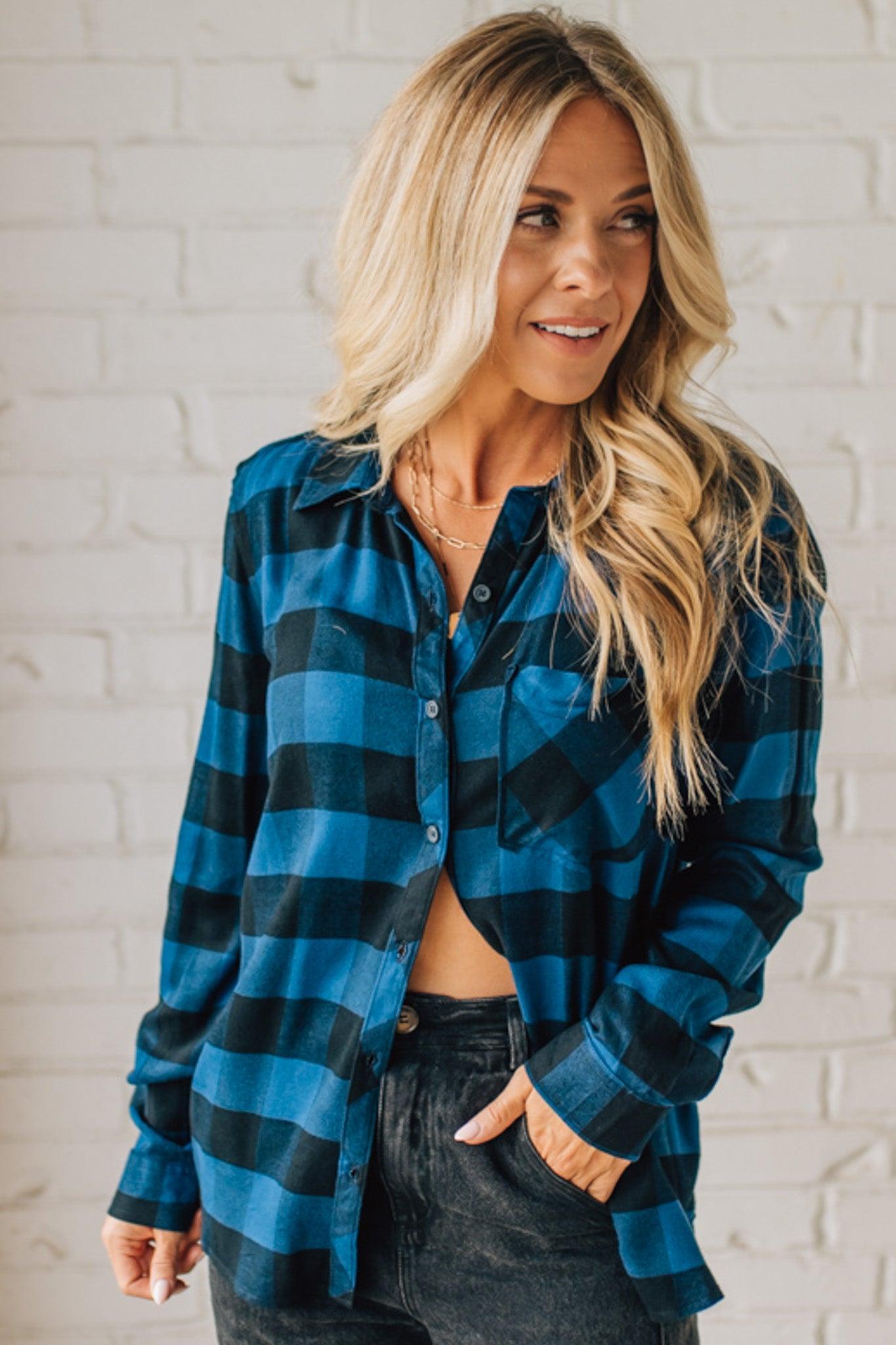 Woman wearing a blue and black checkered shirt against a white brick wall.