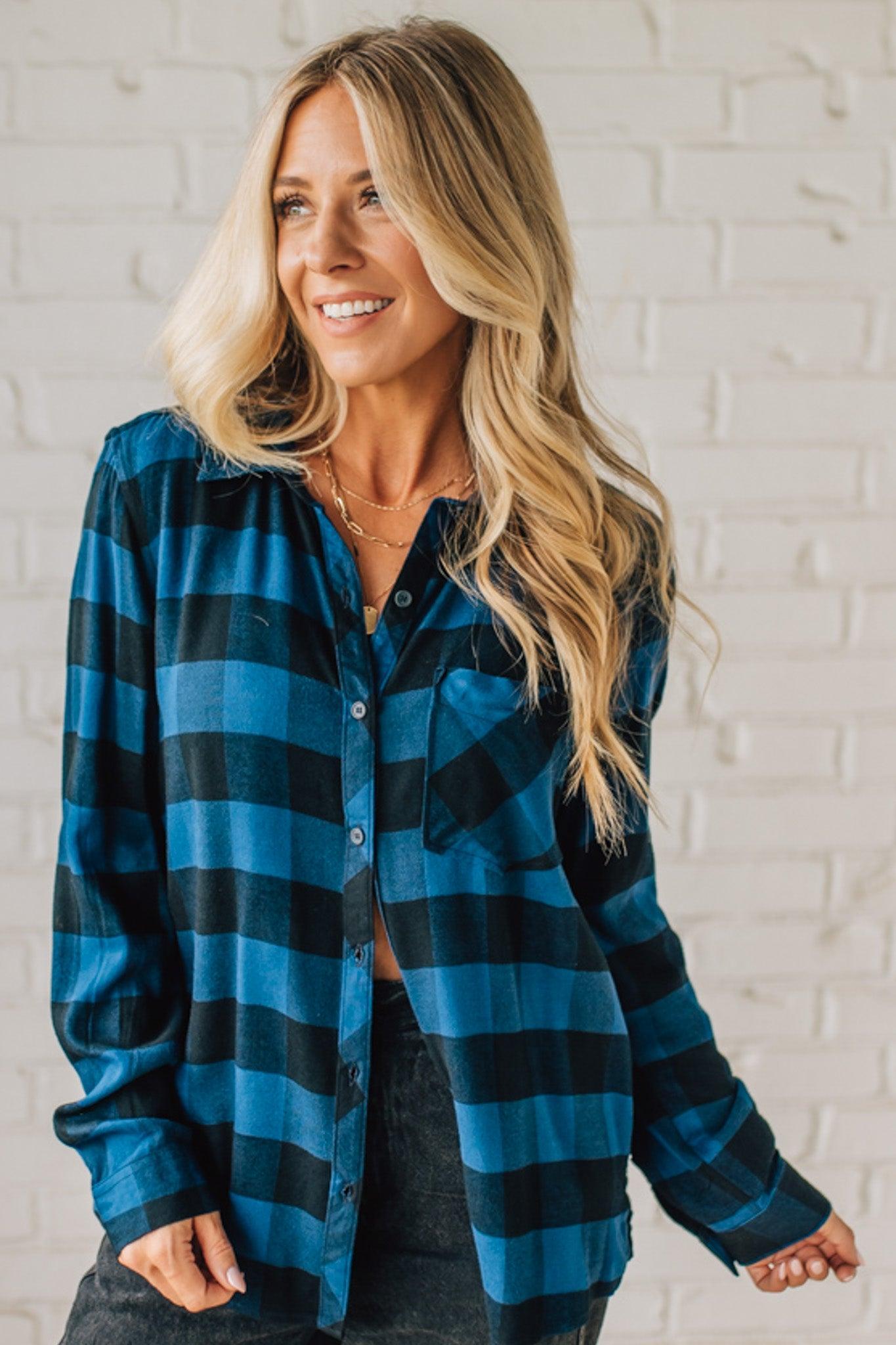 Woman wearing a blue and black plaid shirt against a white brick wall.