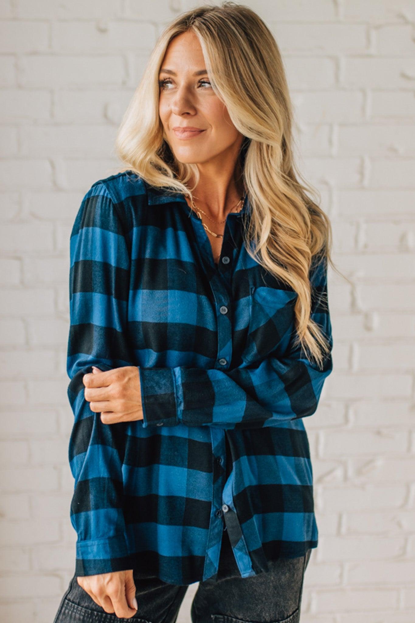Woman wearing a blue and black plaid shirt against a white brick wall.