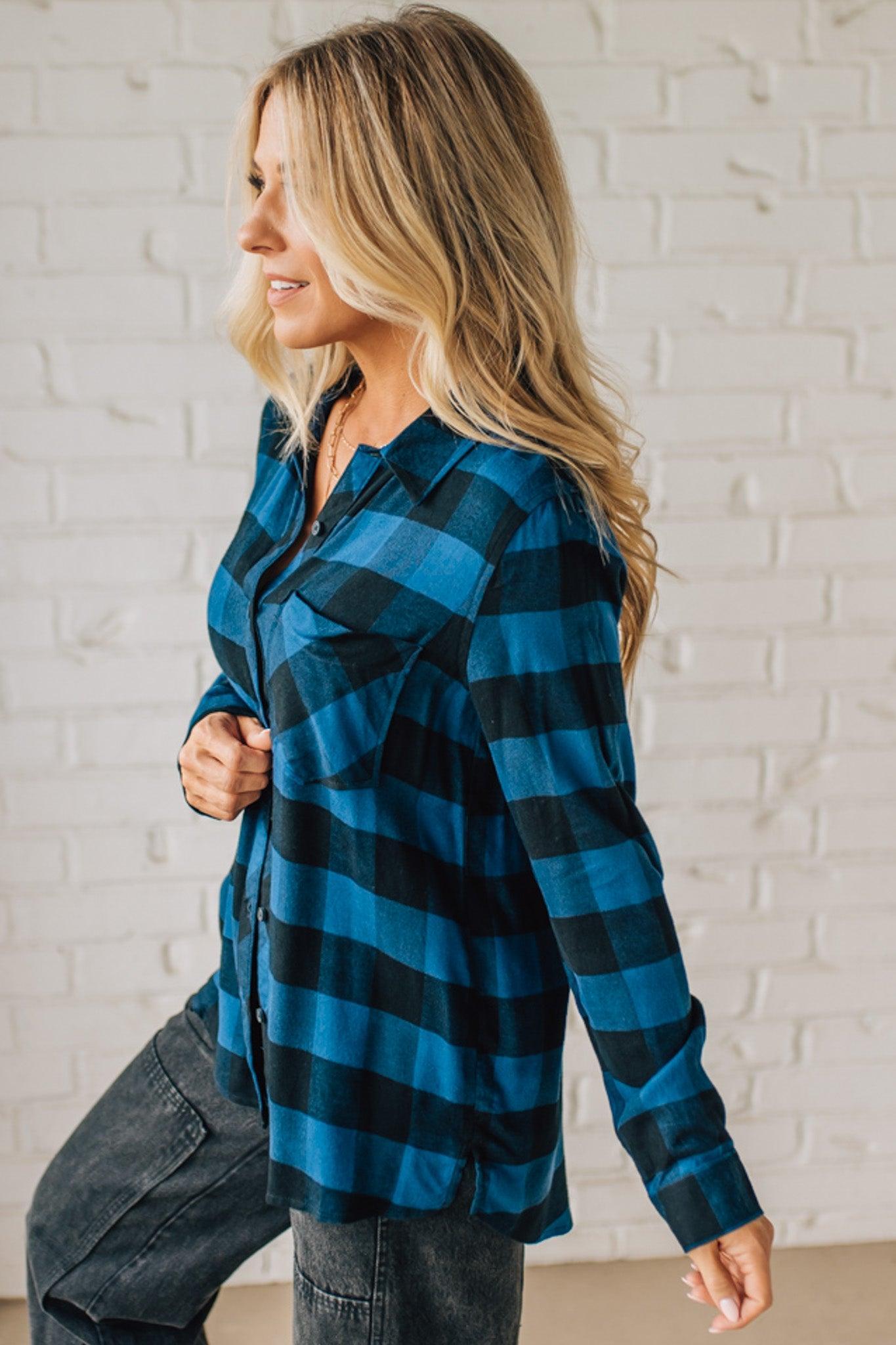 Woman wearing a blue and black plaid shirt against a white brick wall.