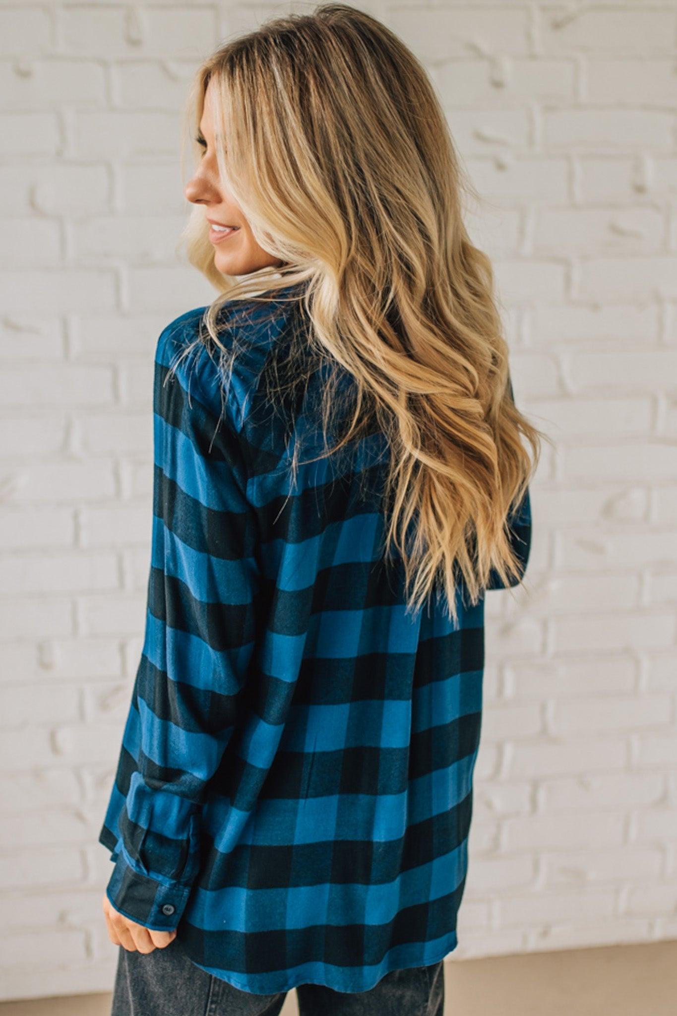 Woman wearing a blue and black checkered shirt against a white brick wall.
