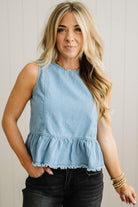 Woman wearing a light blue denim top with ruffled hem against a neutral background