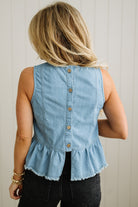 Light blue denim sleeveless top with buttons and ruffled hem worn by a person against a neutral background