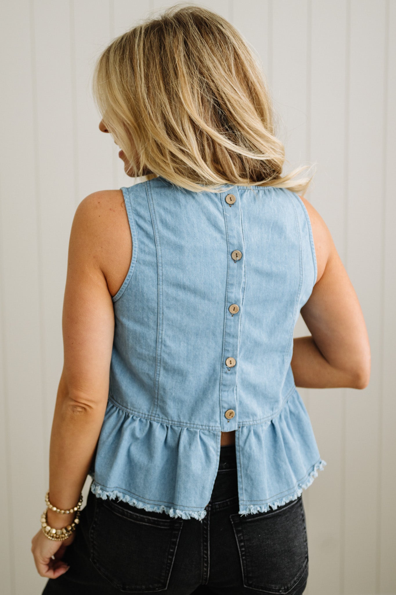 Woman wearing a light blue denim vest with ruffled hem against a neutral background