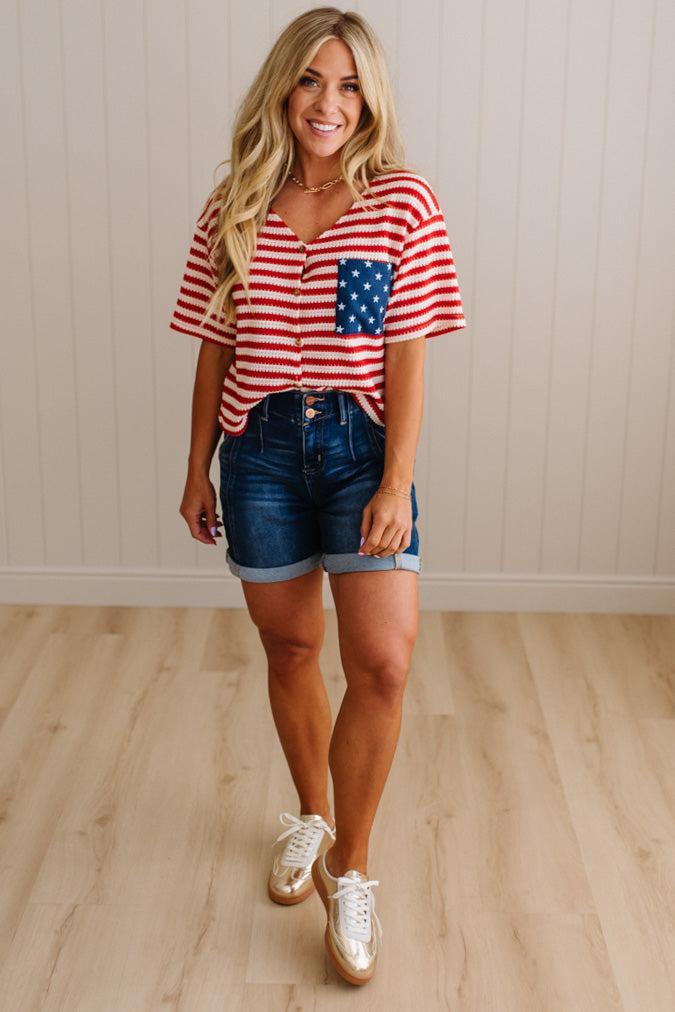 Woman wearing a red, white, and blue striped shirt with an American flag pocket and denim shorts.