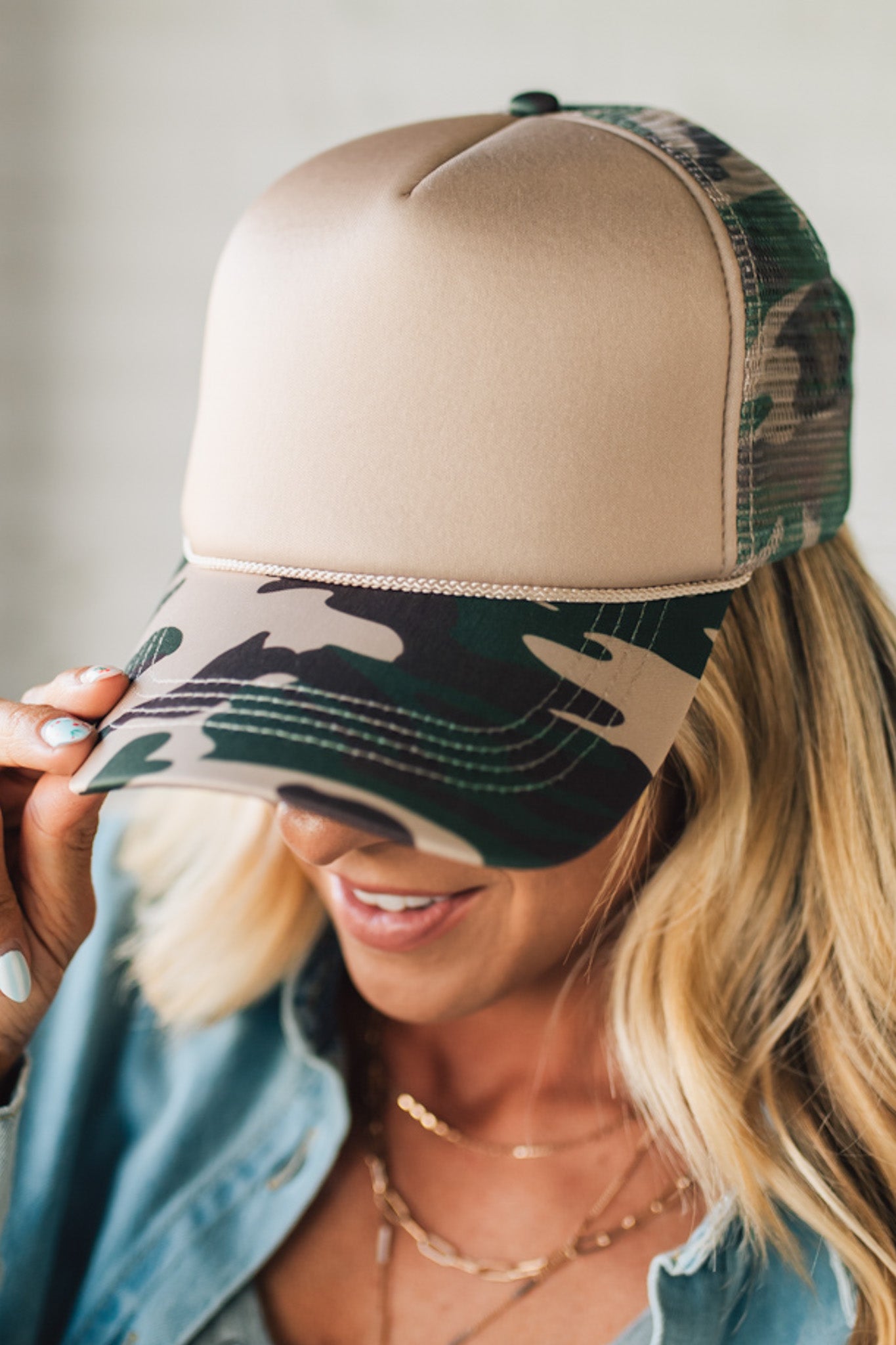 Woman wearing a beige and camouflage trucker hat with a blurred background