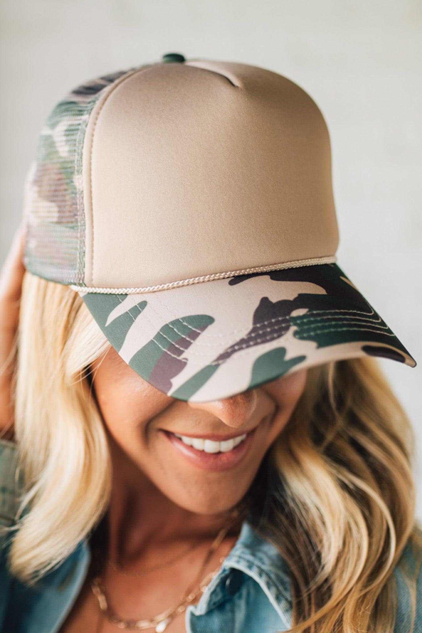 Woman wearing a beige and camouflage baseball cap with a neutral background