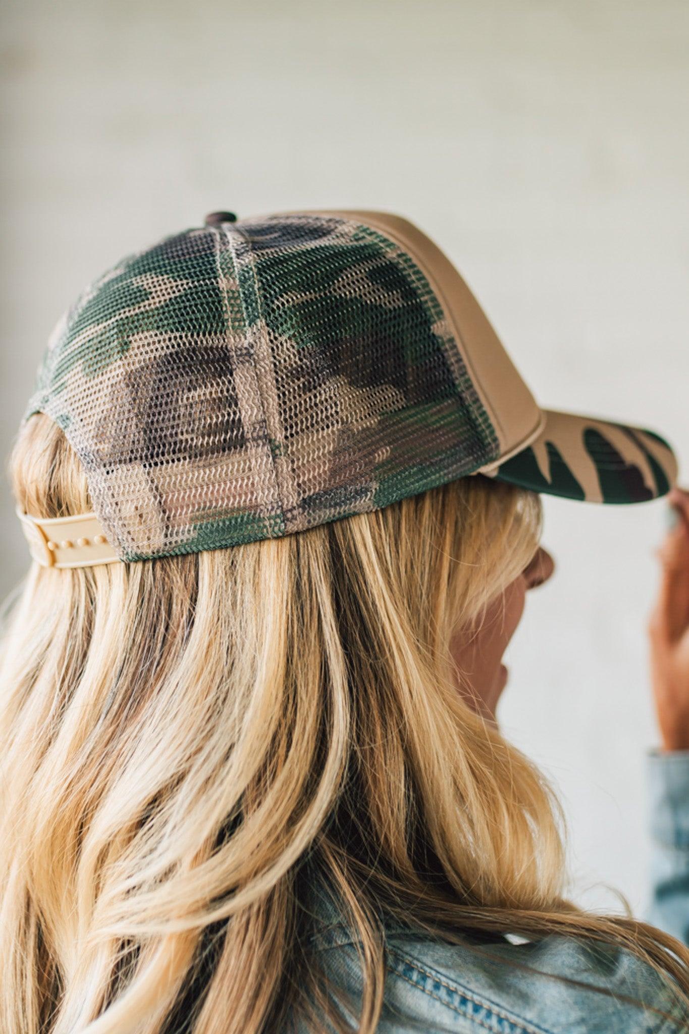 Camouflage trucker hat worn by a person with blonde hair.