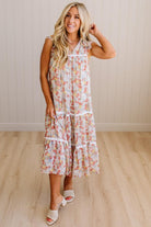Woman wearing a floral dress standing in a room with wooden flooring and a neutral wall.