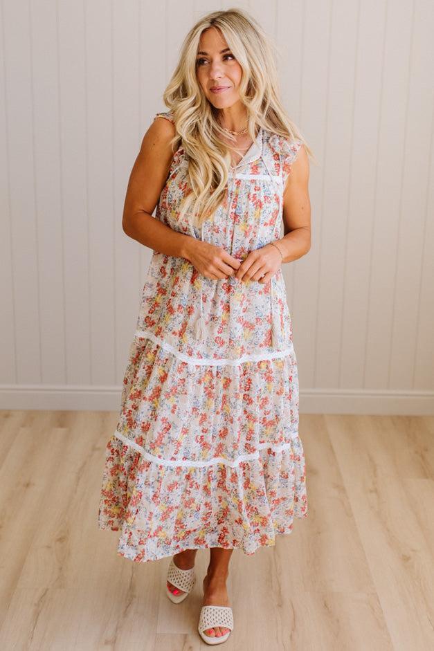 Woman wearing a floral dress standing in a room with wooden flooring and a white wall.