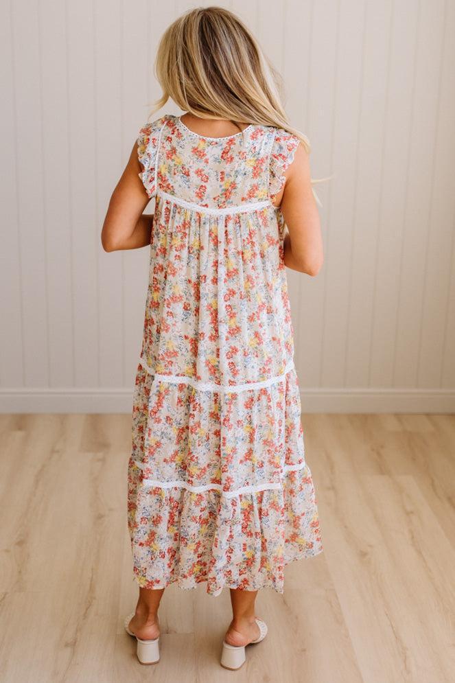 Woman wearing a floral dress standing in a room with wooden flooring and a neutral wall.