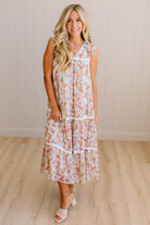 Woman wearing a floral dress standing in a room with wooden flooring and a white wall.