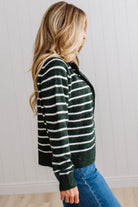 BLONDE WOMAN IN A BRIGHTLY LIT STUDIO WEARING A CREAM TANK AND DARK JEANS SHOWING A OUTSEAMED, LONG SLEEVE, FUZZY, CREW NECK STRIPED BUTTON DOWN SWEATER CARDIGAN IN FOREST GREEN.