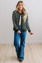 BLONDE WOMAN IN A BRIGHTLY LIT STUDIO WEARING A CREAM TANK AND DARK JEANS SHOWING A OUTSEAMED, LONG SLEEVE, FUZZY, CREW NECK STRIPED BUTTON DOWN SWEATER CARDIGAN IN FOREST GREEN.