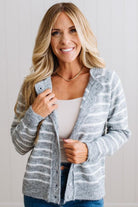 BLONDE WOMAN IN A BRIGHTLY LIT STUDIO WEARING A CREAM TANK AND DARK JEANS SHOWING A OUTSEAMED, LONG SLEEVE, FUZZY, CREW NECK STRIPED BUTTON DOWN SWEATER CARDIGAN IN HEATHER GREY.