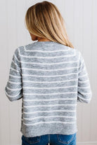 BLONDE WOMAN IN A BRIGHTLY LIT STUDIO WEARING A CREAM TANK AND DARK JEANS SHOWING A OUTSEAMED, LONG SLEEVE, FUZZY, CREW NECK STRIPED BUTTON DOWN SWEATER CARDIGAN IN HEATHER GREY.