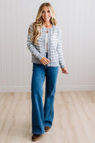 BLONDE WOMAN IN A BRIGHTLY LIT STUDIO WEARING A CREAM TANK AND DARK JEANS SHOWING A OUTSEAMED, LONG SLEEVE, FUZZY, CREW NECK STRIPED BUTTON DOWN SWEATER CARDIGAN IN HEATHER GREY.