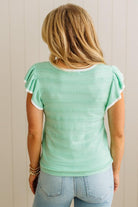 Person wearing a light green top with ruffled sleeves against a neutral background