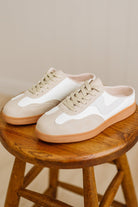 Pair of white sneakers with brown soles on a wooden stool against a neutral background