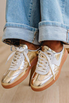Woman wearing metallic gold and white slip-on sneakers featuring a bold swoosh pattern on the side, giving them a dynamic, sporty look. The durable gum sole provides excellent traction and a retro touch.