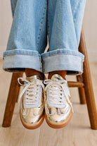 Woman wearing metallic gold and white slip-on sneakers featuring a bold swoosh pattern on the side, giving them a dynamic, sporty look. The durable gum sole provides excellent traction and a retro touch.
