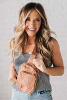 BLONDE WOMAN WEARING A SCOOP NECK, SLEEVELESS, TEXTURED BLACK AND WHITE STRIPE TANK TOP WITH CAMEL CROSSBODY BAG.