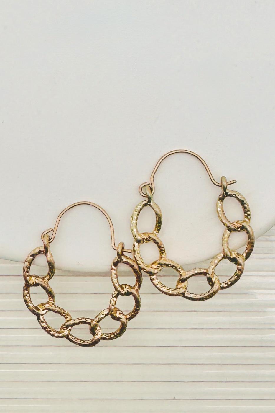 Gold chain earrings on a textured stone surface