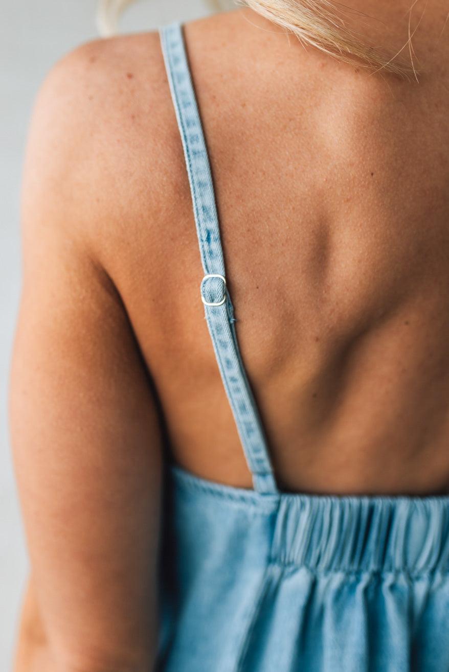 Blonde woman wearing a long denim maxi dress with adjustable spaghetti straps, side pockets, and a side slit.