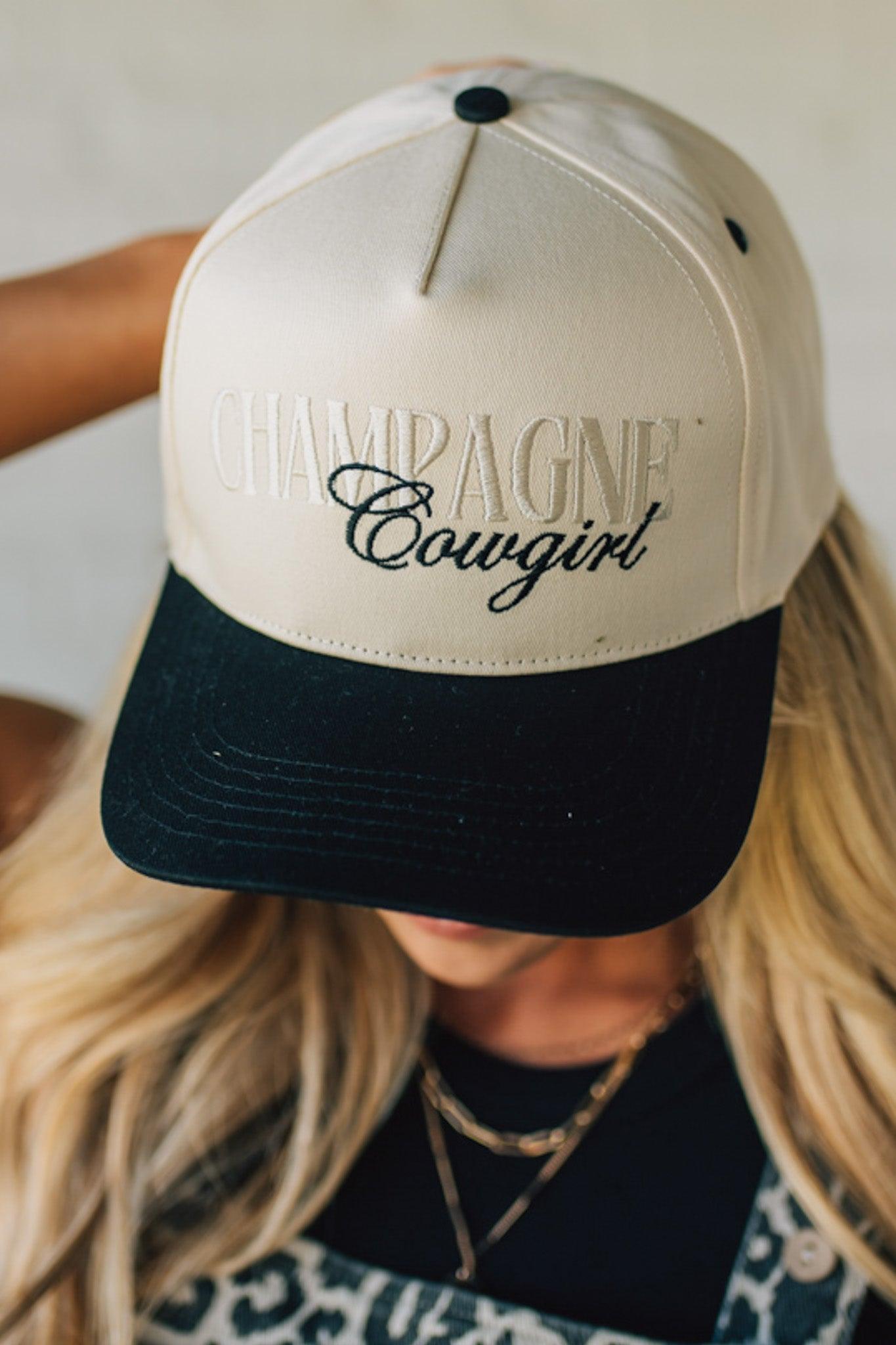 Blonde woman wearing a cream and black trucker hat with "Champagne Cowgirl" embroidered at the front.