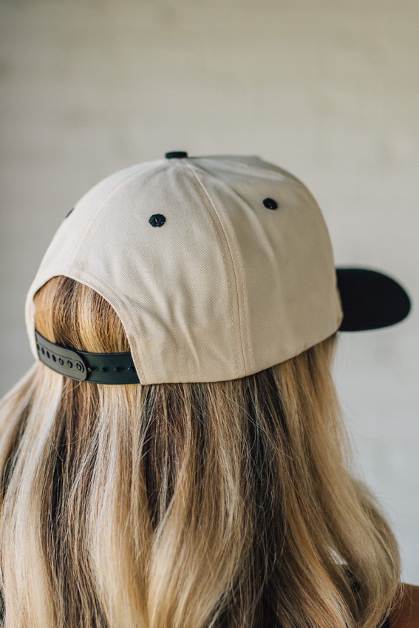 Blonde woman wearing a cream and black trucker hat with "Champagne Cowgirl" embroidered at the front.