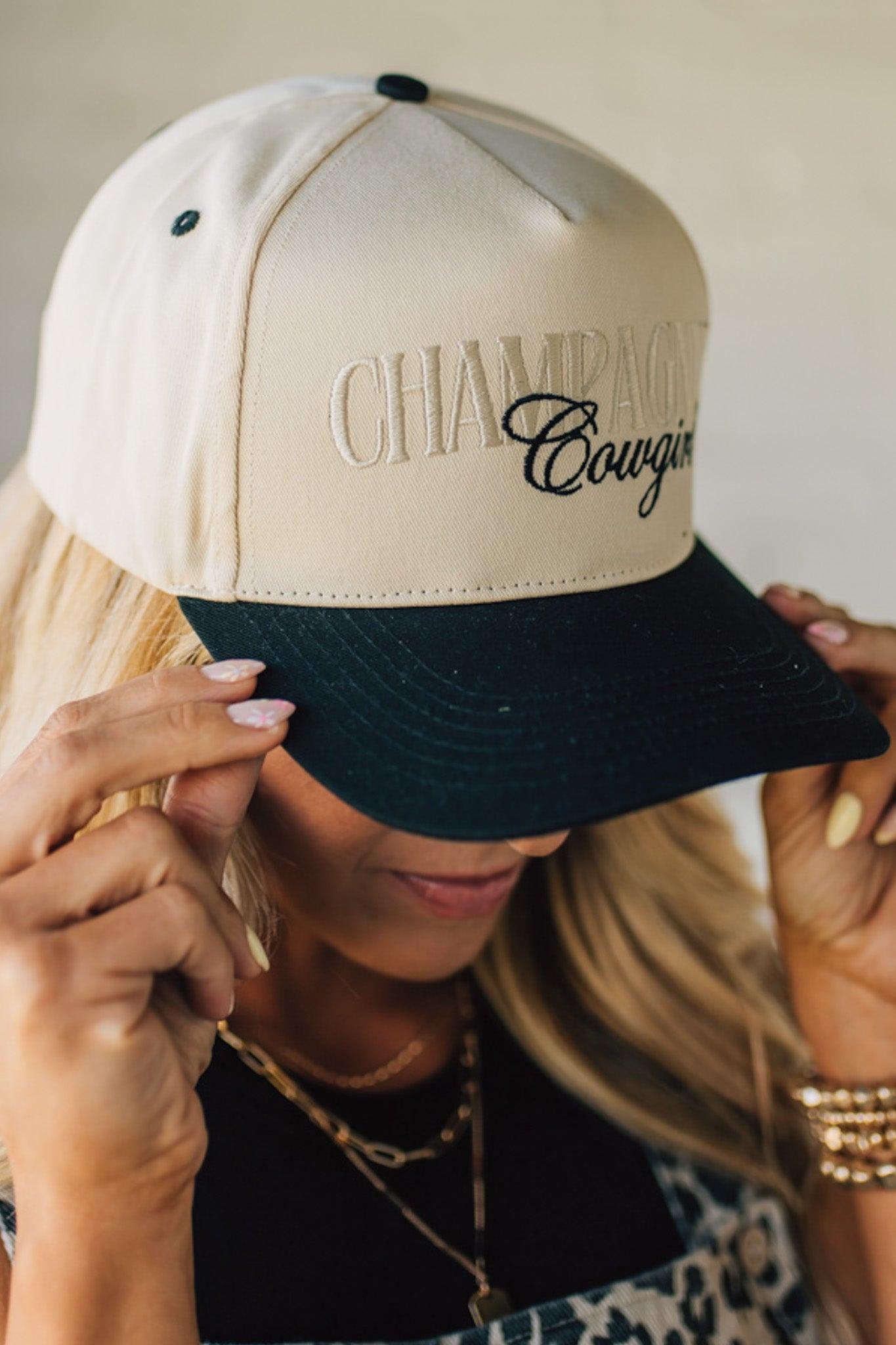 Blonde woman wearing a cream and black trucker hat with "Champagne Cowgirl" embroidered at the front.