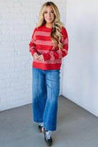 Woman wearing a red and white striped sweater and blue jeans against a white brick wall.