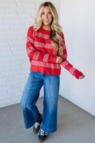 Woman wearing a red and white striped sweater and blue jeans against a white brick wall.