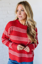 Woman wearing a red sweater with white stripes against a white brick wall.