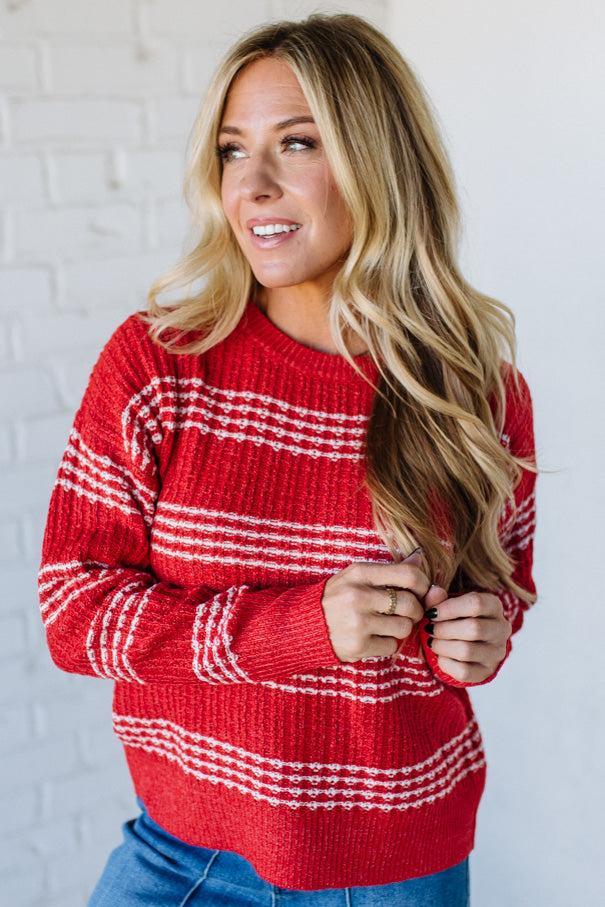Woman wearing a red and white striped sweater against a white brick wall.