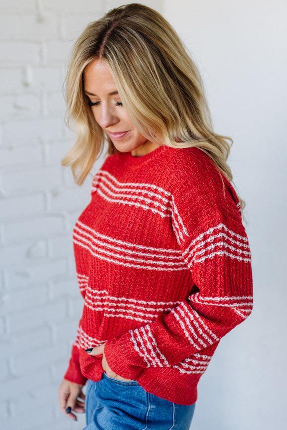 Woman wearing a red and white striped sweater against a white brick wall.