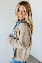 Woman wearing a beige cardigan with a denim trim with a white background
