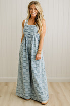 Woman wearing a blue patterned jumpsuit standing against a white paneled wall.
