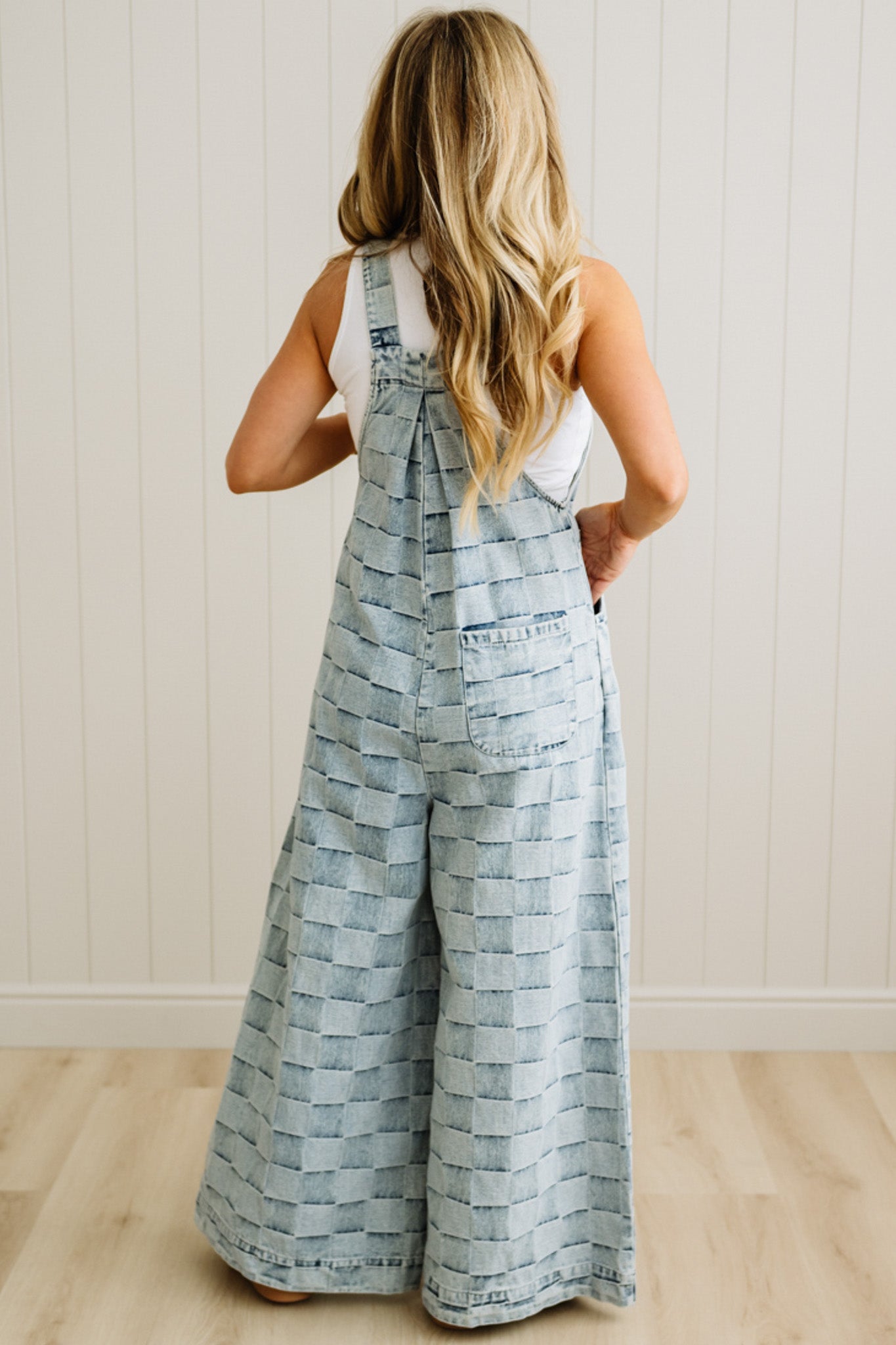 Woman wearing a patterned denim jumpsuit against a white paneled wall.