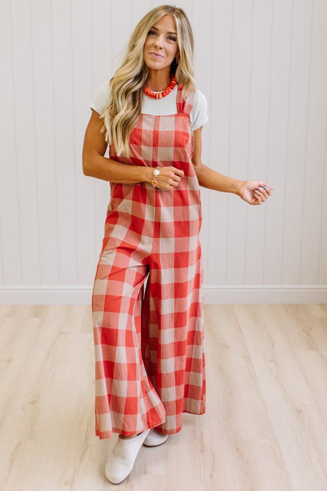 Blonde woman in a studio with light wood floors and a light backdrop, wearing a tee-shirt and latte/orage wide leg jumpsuit.
