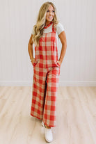 Blonde woman in a studio with light wood floors and a light backdrop, wearing a tee-shirt and latte/orage wide leg jumpsuit.