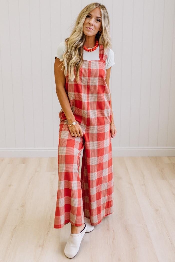 Blonde woman in a studio with light wood floors and a light backdrop, wearing a tee-shirt and latte/orage wide leg jumpsuit.