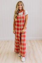 Blonde woman in a studio with light wood floors and a light backdrop, wearing a tee-shirt and latte/orage wide leg jumpsuit.