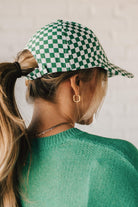 Blonde woman wearing a green and white checkered ball cap. 