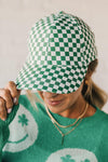 Blonde woman wearing a green and white checkered ball cap. 