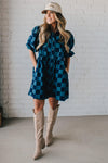 Blonde woman wearing a hat and boots with checkered denim knee length dress.