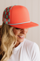 Person wearing a red cap with plaid side panel on a beige background