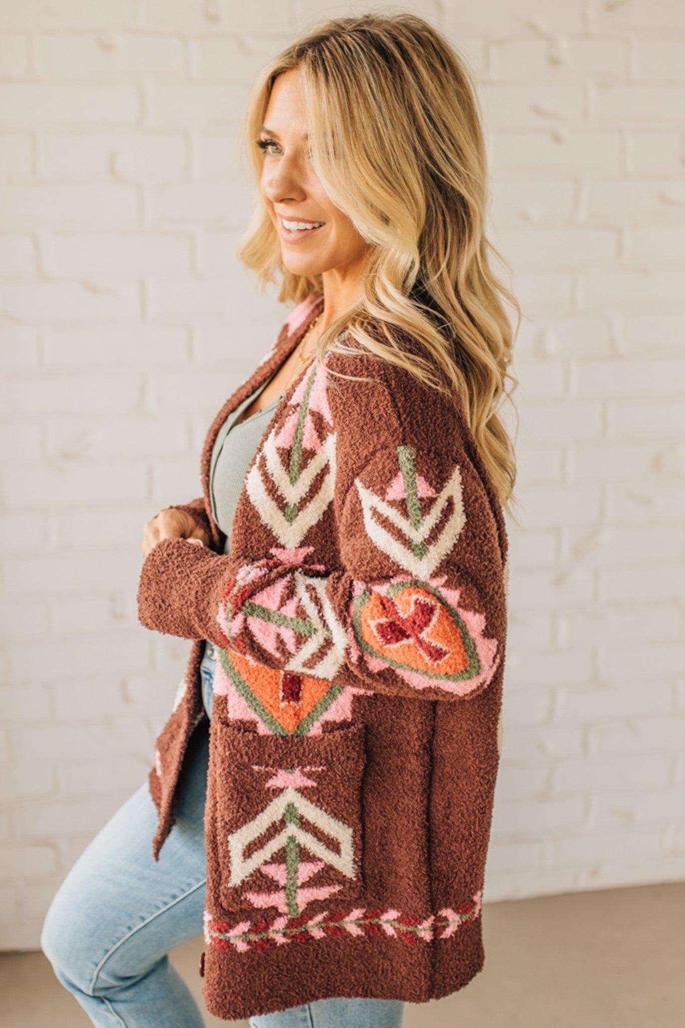 Woman wearing a patterned brown cardigan against a white brick wall.