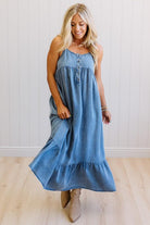 Woman wearing a blue denim dress standing against a white wall.